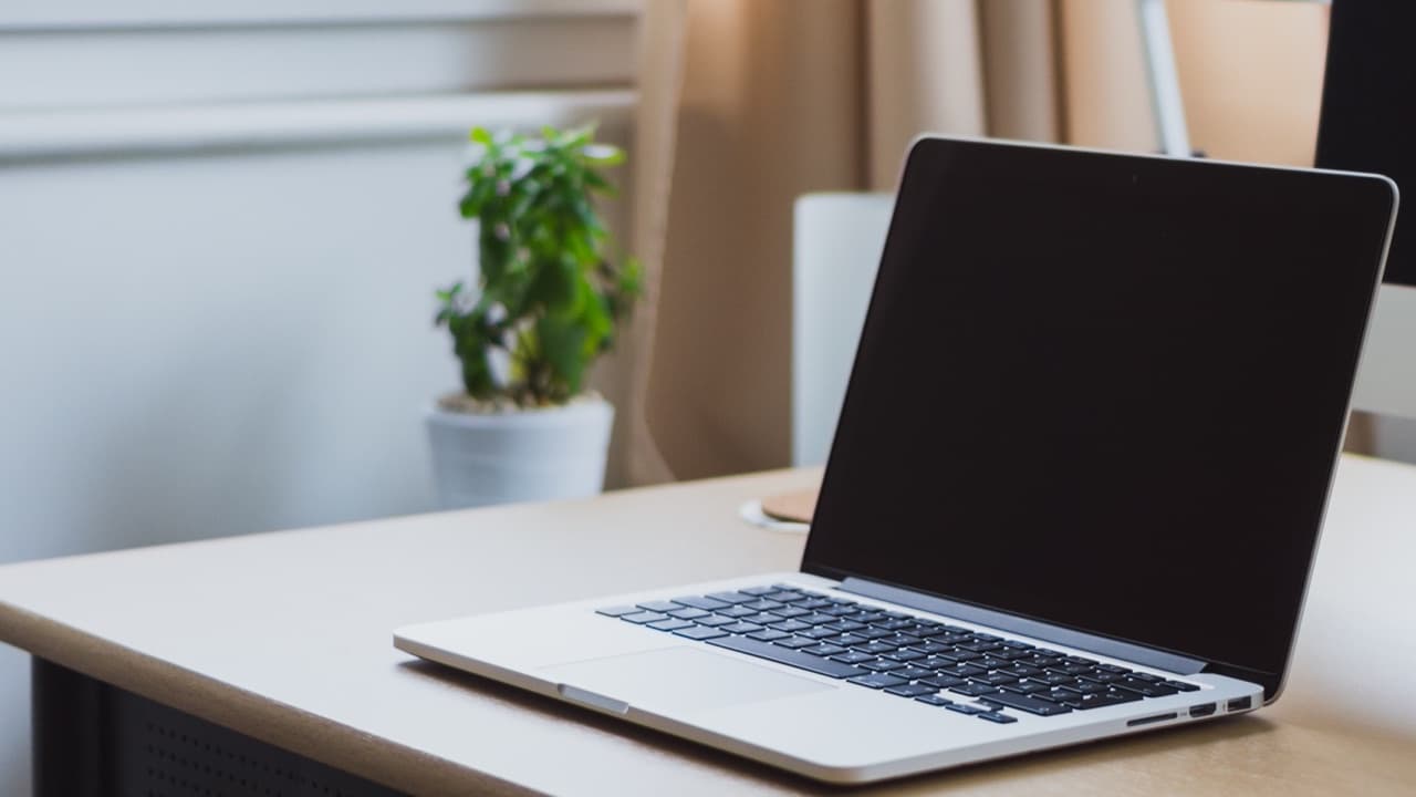 A laptop with a blank screen on a wooden desk beside a window