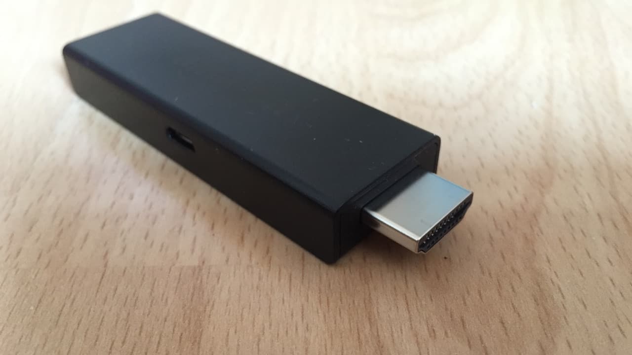 A black HDMI streaming stick on a wooden desk
